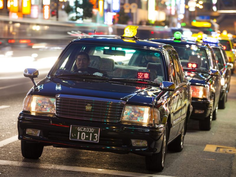 "Osaka, Japan - February 6, 2012: Black taxis stand in a row at the lights in Umeda Osaka. A driver sits in the vehicle."