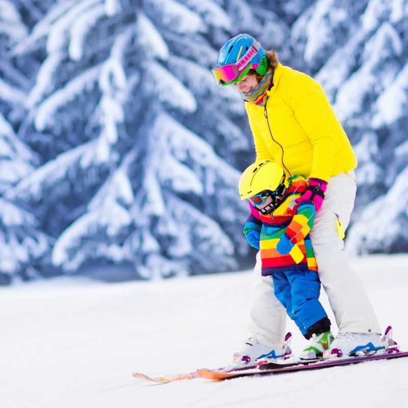 Mother and little child skiing in Alps mountains. Active mom and toddler kid with safety helmet, goggles and poles. Ski lesson for young children. Winter sport for family. Little skier racing in snow